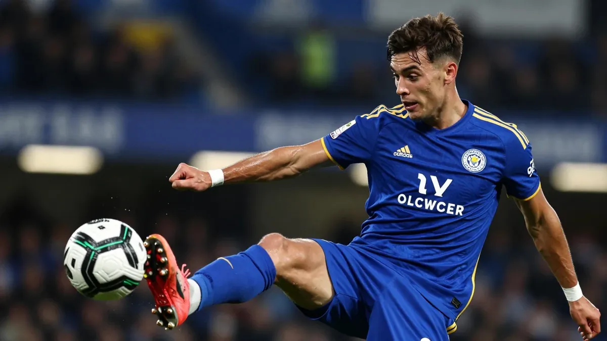 A young, lean midfielder in his mid-20s, dressed in Leicester City's blue and amber home kit with the club's crest...