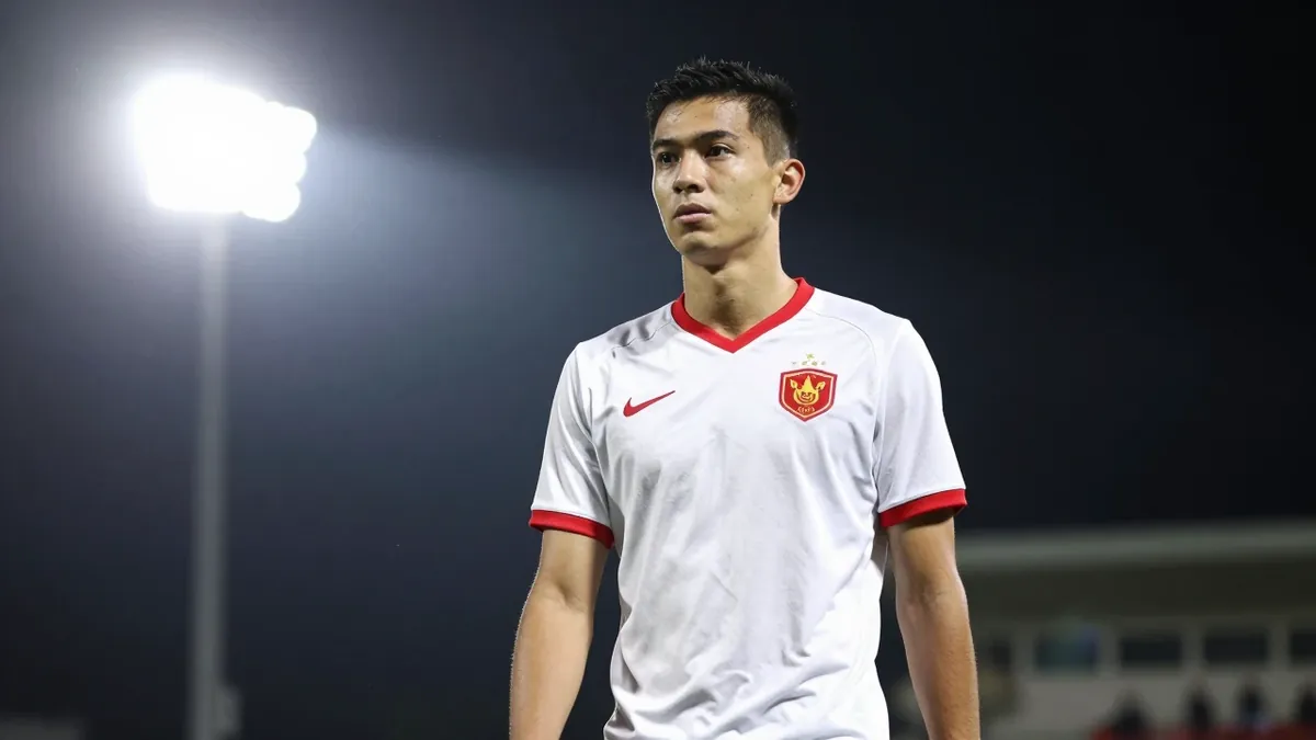 19-year-old centre-back, lean build, standing 6ft 6in, in a clean white jersey with red trim, tight action crop, focused gaze