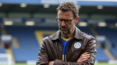 A medium shot of a 45-year-old, ruggedly-built, bespectacled Leicester City manager with a worn expression, his 5'9"...